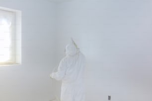 Worker painting wall with Airless Spray Gun in white color.