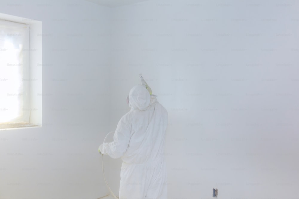 Worker painting wall with Airless Spray Gun in white color.