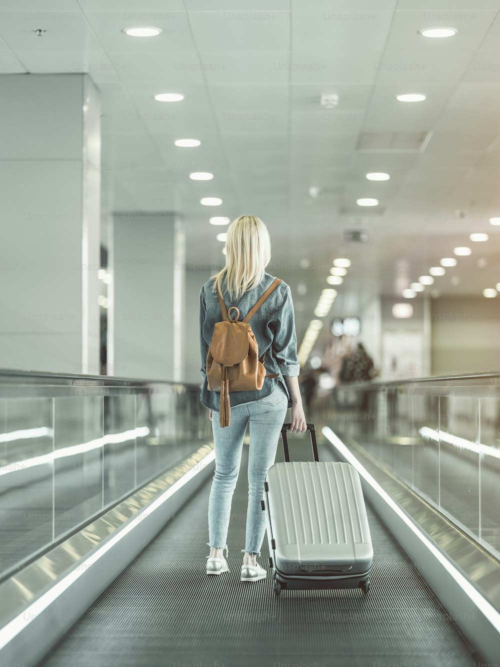 Full length female keeping big suitcase on escalator in airport. Tourist during journey concept