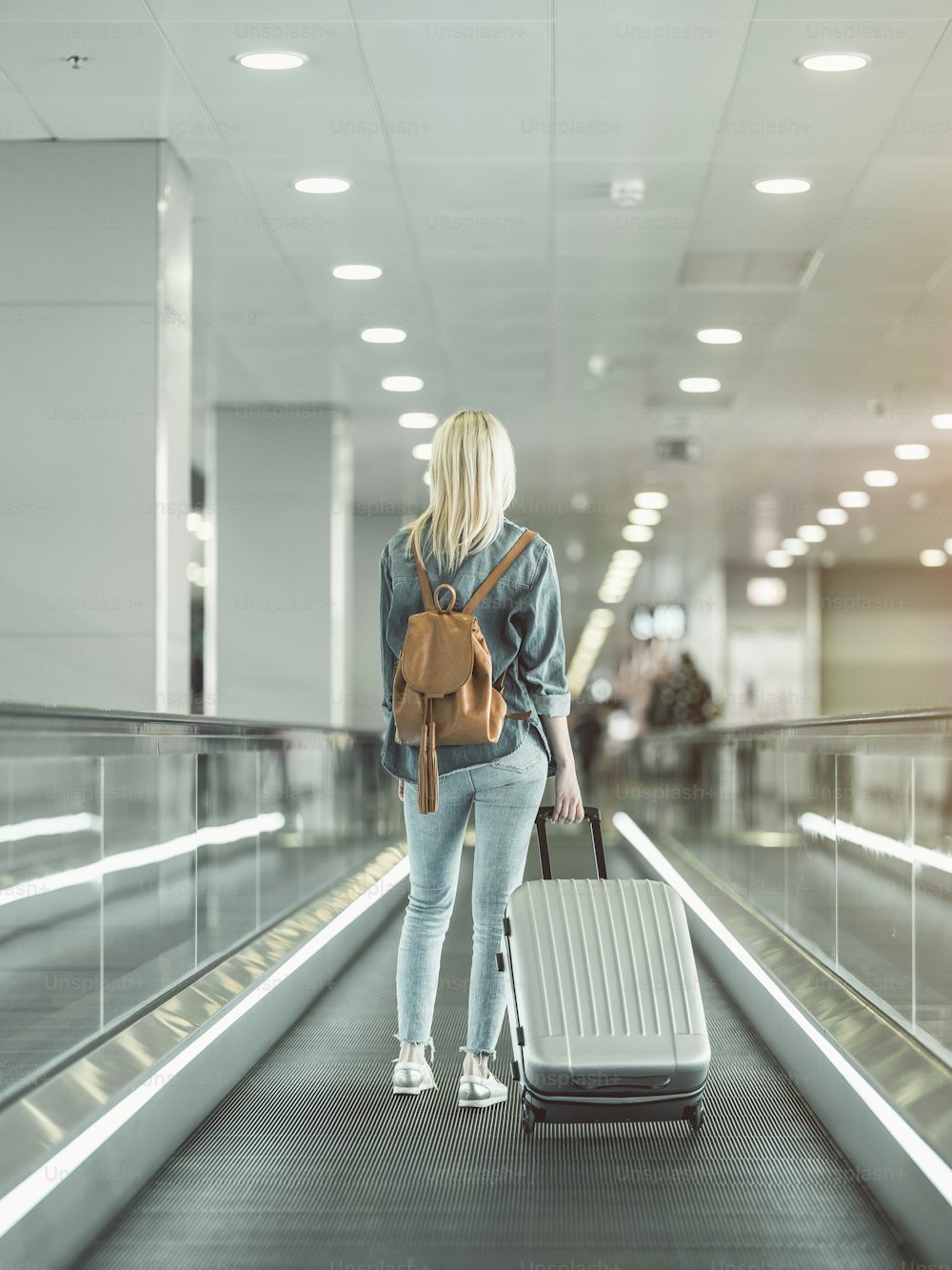 Fêmea de comprimento total mantendo mala grande na escada rolante no aeroporto. Conceito de turista durante a viagem
