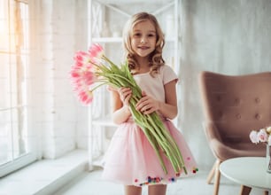 Little cute girl with bouquet of pink tulips at home. Happy Mother's Day!