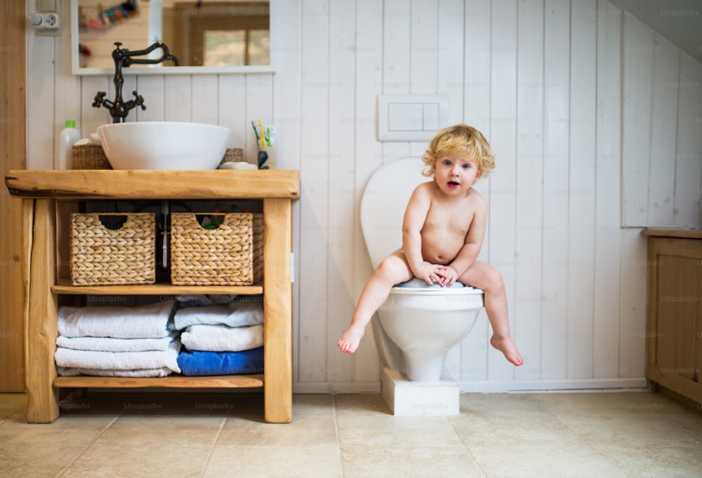 Criança bonita no banheiro. Garotinho sentado no vaso sanitário.