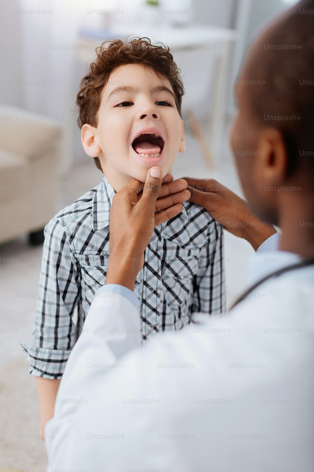 Arztdiagnose. Junge, der den Mund öffnet, und erfahrener professioneller männlicher Arzt, der sein Kinn berührt