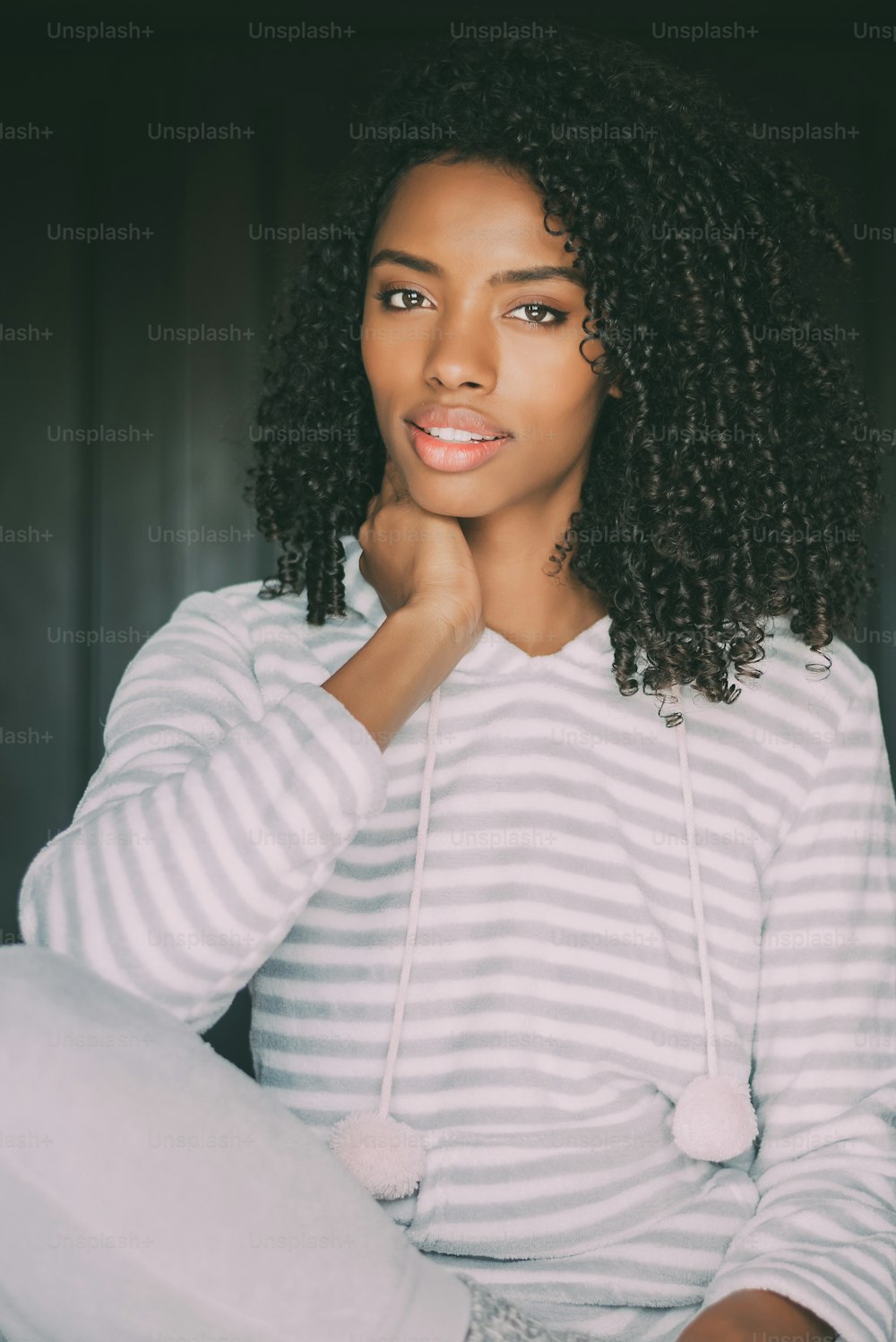 portrait of a pretty black woman with curly hair smiling sit on bed looking at the camera