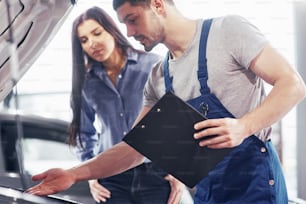 Un meccanico uomo e una cliente donna guardano il cofano dell'auto e discutono delle riparazioni.