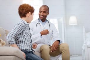 Elementary biology. Pleased appealing male doctor and boy sitting on couch while talking and smiling