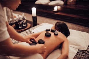 Una joven atractiva se relaja en el spa y el centro de bienestar mientras recibe un masaje con piedras. Concepto de tratamiento de belleza.
