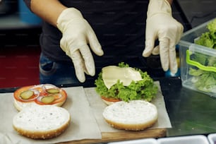 processo di preparazione dell'hamburger. Lo chef con le mani in guanti cuoce hamburger e cheeseburger, mettendo gli ingredienti sulla scrivania di legno. Catering nella food court del Mall Concept