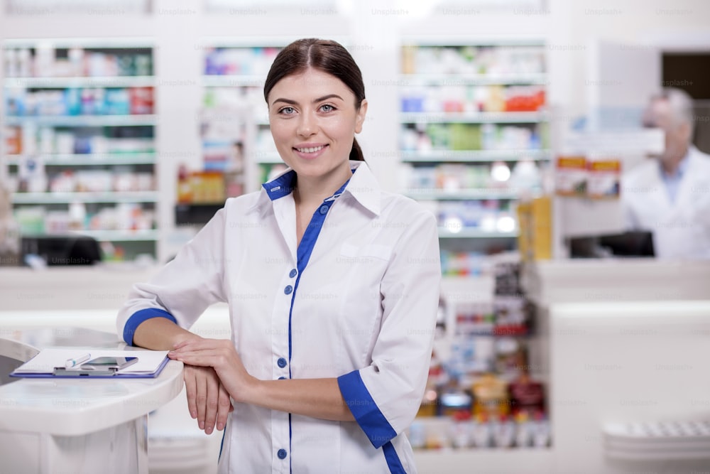 Come to us. Happy female pharmacist posing in drugstore while looking at camera