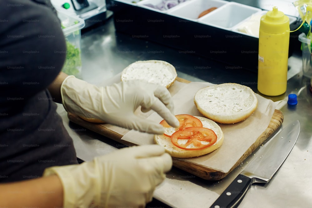 process of making burger. chef hands in gloves cooking hamburgers and cheeseburgers, putting ingridients on wooden desk. catering in food court at mall concept