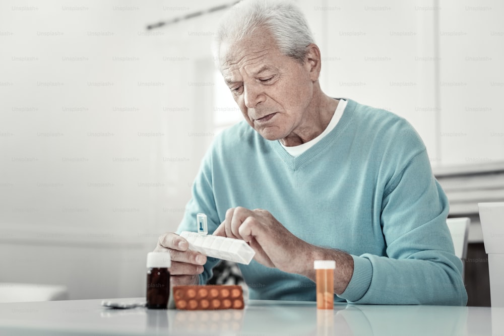 それは役に立ちます。集中した年配の真面目な男は、錠剤のパックを持ってテーブルのそばに座り、それに集中しています。