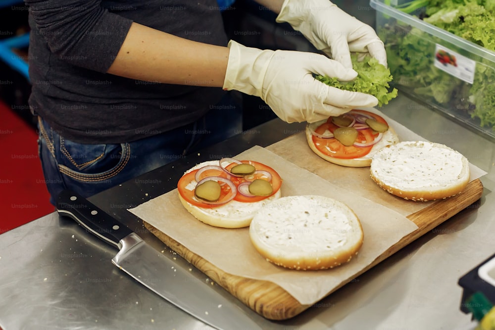 process of making burger. chef hands in gloves cooking hamburgers and cheeseburgers, putting ingridients on wooden desk. catering in food court at mall concept