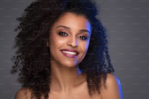 Retrato de beleza de mulher jovem de pele escura sorridente com cabelo afro encaracolado e maquiagem glamourosa. Foto de estúdio em fundo cinza, espaço de cópia.