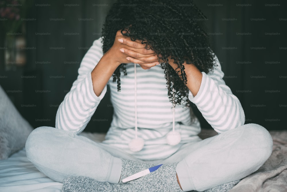 mujer negra pensativa, preocupada y triste con la prueba de embarazo en la cama