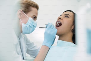 Cuidado de los dientes. Paciente bastante seria sentada con la boca abierta mientras el dentista examina sus dientes