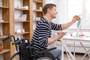 Making portrait. Handsome invalid male sitting on his wheelchair while painting