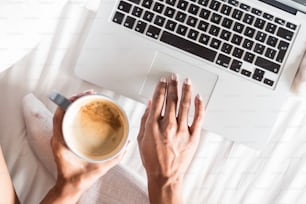 ベッドの上でパソコンを飲みながらコーヒーを飲むタイツ姿の女性