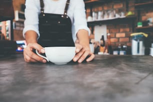 Foto cortada de barista no avental segurando xícara de café no balcão no café. Inicie o conceito de comida e bebida de pequeno empresário.