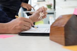 사무실에서 계약 계약에 서명하는 동안 고객에게 집 열쇠를 들고 있는 부동산 중개인, 부동산에 대한 개념, 집으로 이사하거나 부동산을 임대하는 동안