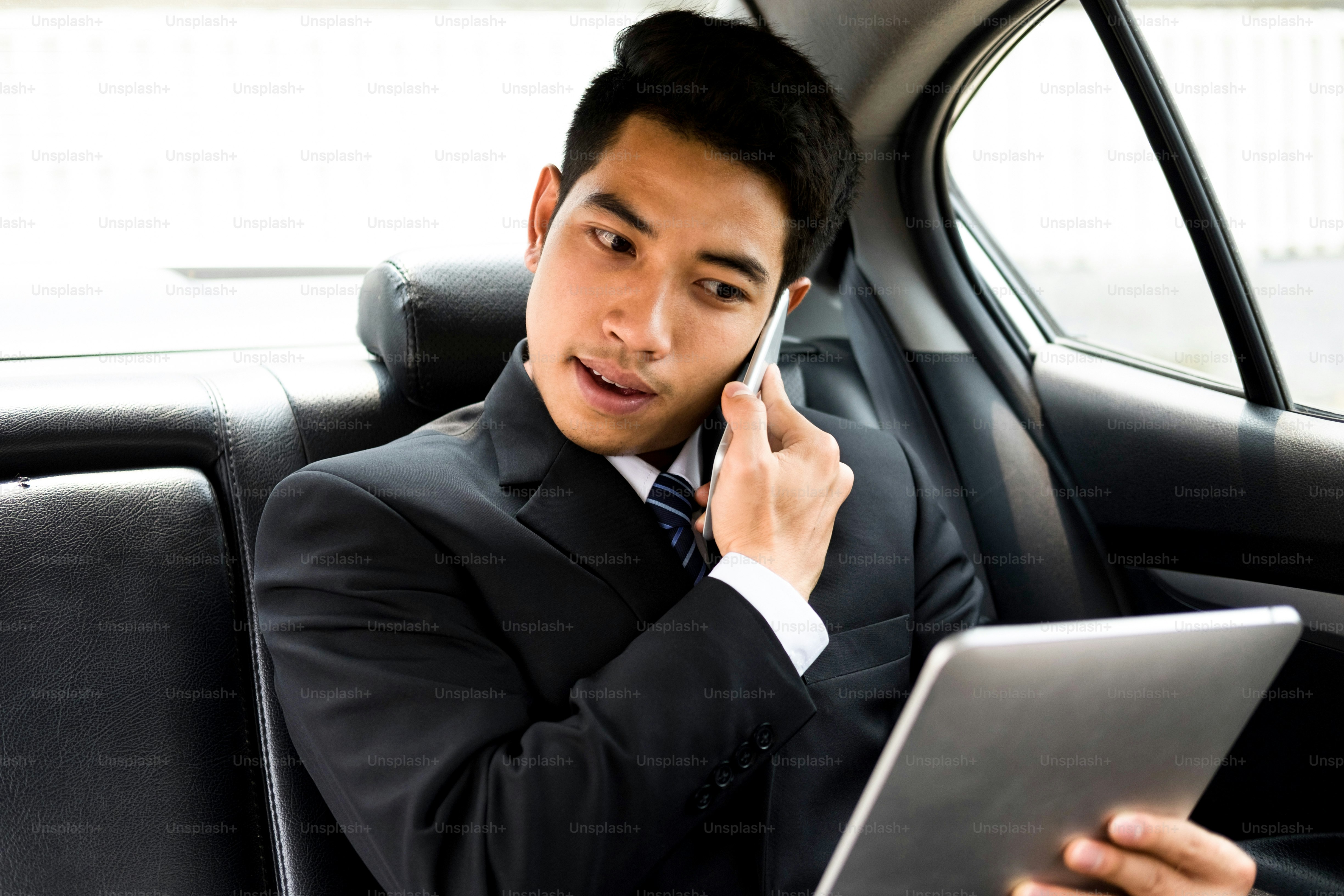 Empresário ocupado usando telefone celular e tablet no carro. Conceito de Online Business e Mobile Office.