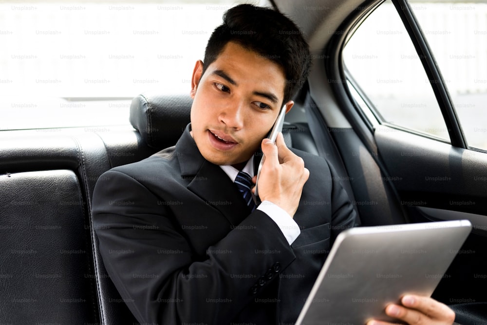 Hombre de negocios ocupado que usa el teléfono móvil y la tableta en el automóvil. Negocio en línea y concepto de oficina móvil.