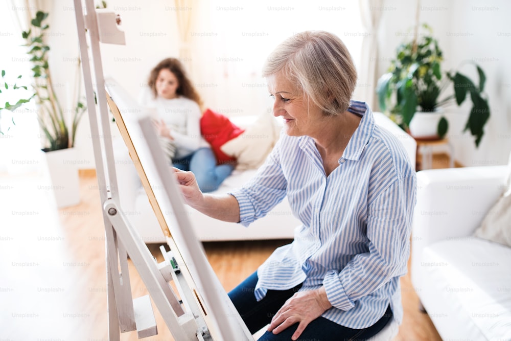 A mother or a grandmother with a teenage girl at home, painting. Family and generations concept.