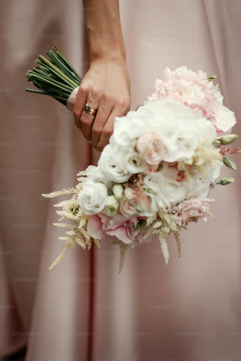 wedding bouquet of pink roses and white flowers. bride holding in hand with luxury rings on background of pink rich dress