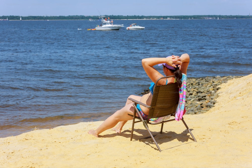 Side view of woman sitting on chair at the beach. Young woman in bikini is relaxing on the seaside.