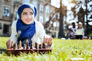 Was wenn. Extrem hübsches muslimisches Mädchen, das an etwas Angenehmes denkt, während es auf Gras liegt und alleine Schach spielt.