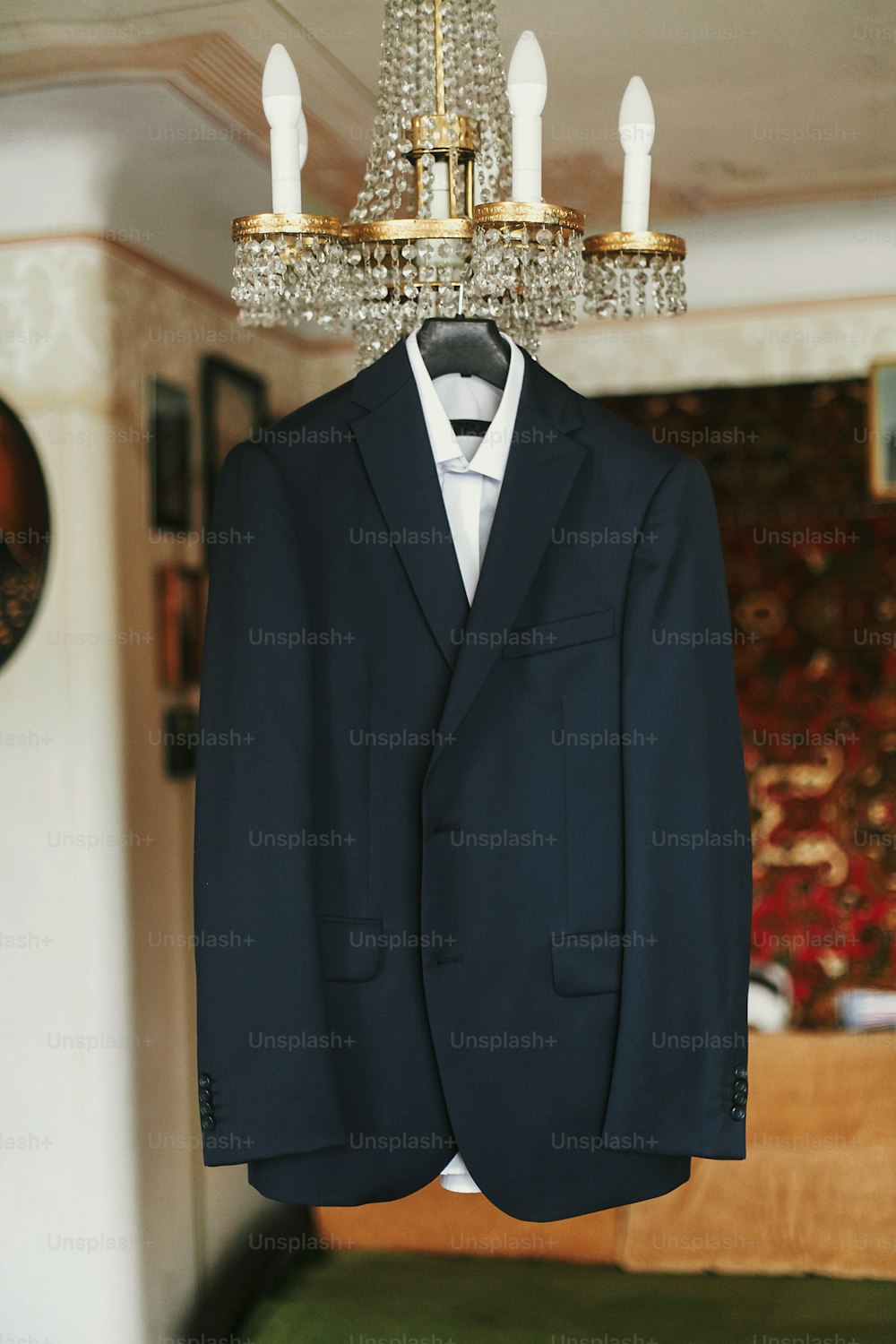stylish black suit with white shirt and bow tie on hanger on luxury chandelier. morning preparations before wedding day. groom outfit