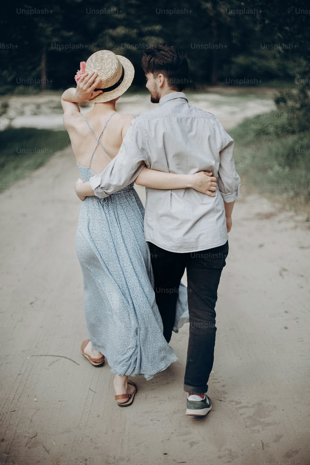 여름 공원에서 산책하는 세련된 힙스터 커플. 남자와 여자는 서로를 껴안고 즐기고 휴식을 취합니다. 세련된 현대 드레스와 밀짚 모자를 쓴 소녀. 소박한 결혼식 개념