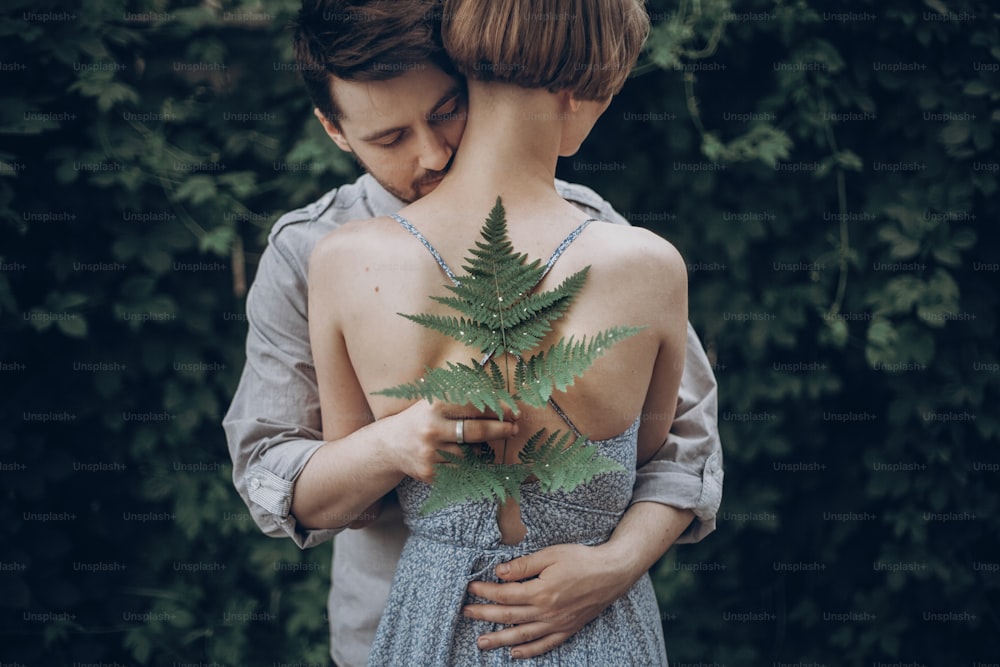 세련된 힙스터 신부와 신랑이 푸른 잎 숲에 포옹하고 있다. 여자 목에 키스하는 남자. 여름 공원에서 사랑에 포옹하는 커플. 관능적 인 낭만적 인 순간. 창조적 인 소박한 결혼식 개념