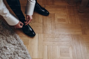groom tying shoes, getting ready in the morning on wooden floor. hotel room. preparation for wedding ceremony. space for text