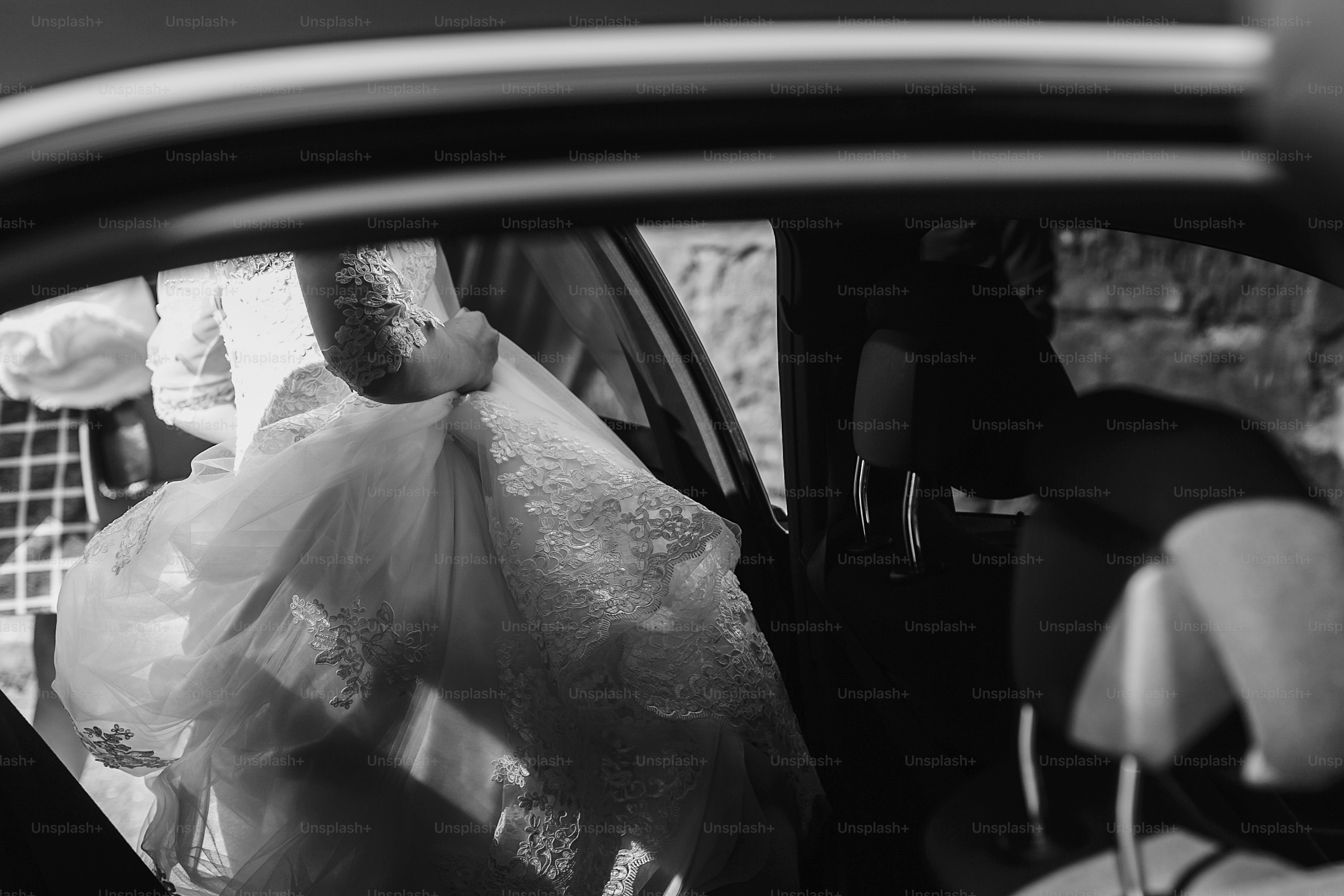 moment of bride in luxury wedding dress getting in car. bride in lace gown sitting in stylish car. black and white photo