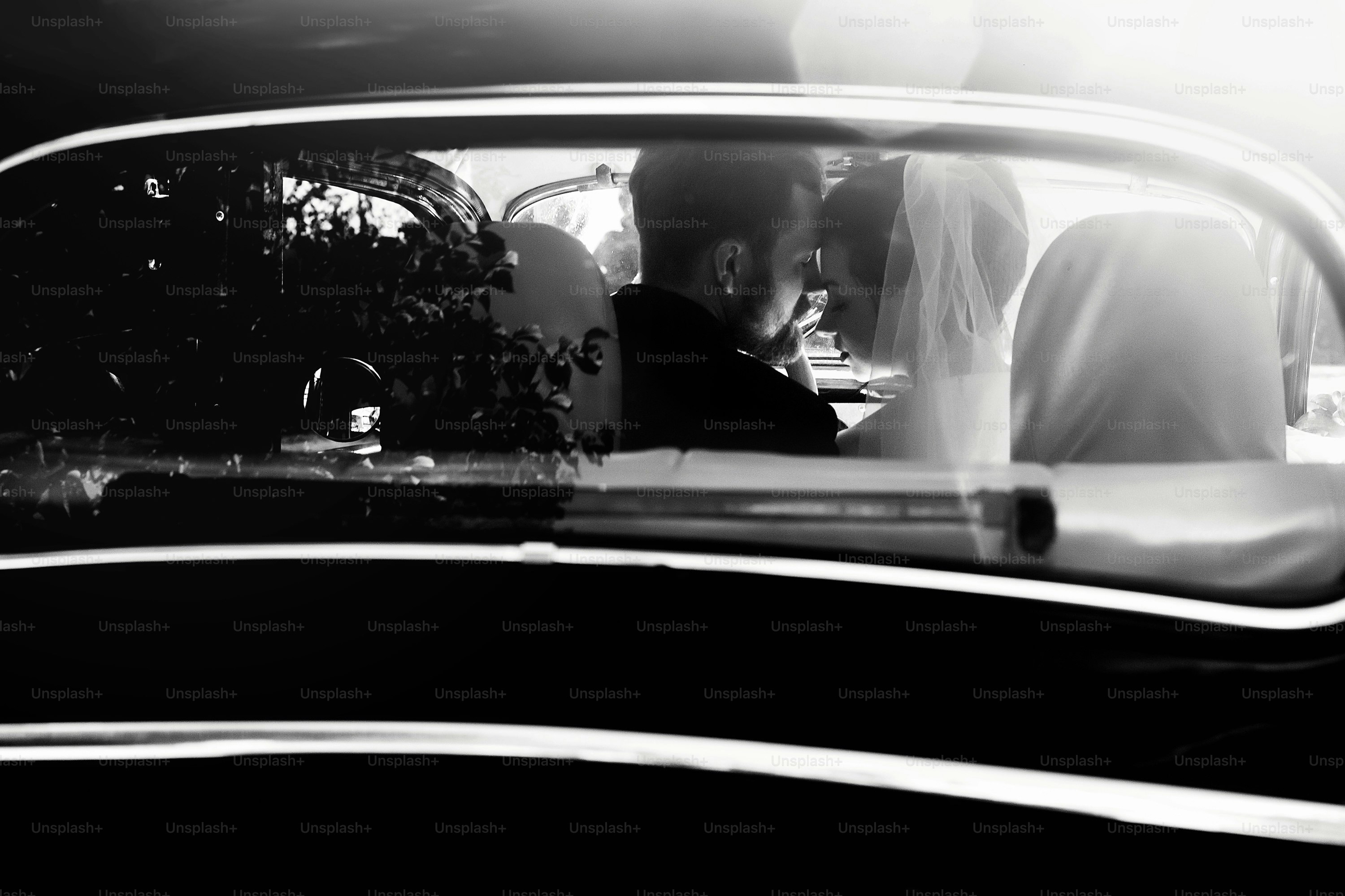 Pareja de bodas elegante de lujo que se abraza en un elegante automóvil negro a la luz. Vista inusual desde atrás. Hermosa novia y guapo novio en estilo retro. foto en blanco y negro