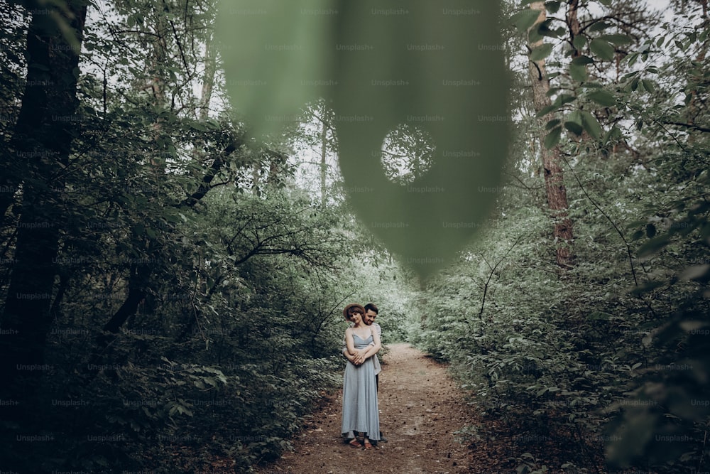 Stilvolle Hipster-Braut und Bräutigam posieren im grünen Sommerwald. Glückliches verliebtes Paar, modernes Outfit, umarmend und entspannend. romantischer Moment. Rustikales Hochzeitskonzept