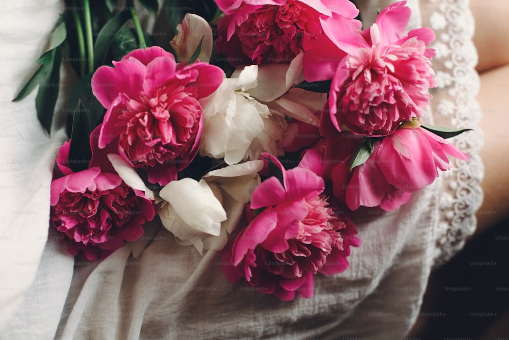 Foto hermosas peonías rosas en las piernas de una chica boho con vestido  bohemio blanco. espacio para texto. elegante mujer hipster sentada con  flores en la mañana malhumorada. momento sensual atmosférico –