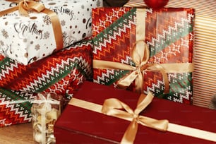 Christmas presents wrapped in colorful gift boxes and golden ribbons, lying on the wooden floor background under green christmas tree with silver ornament decoration, greeting card concept