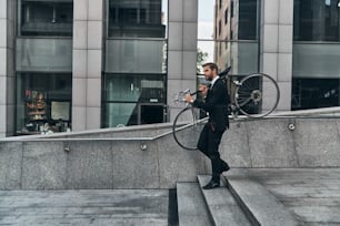 Full length of young man in full suit carrying his bicycle while walking outdoors