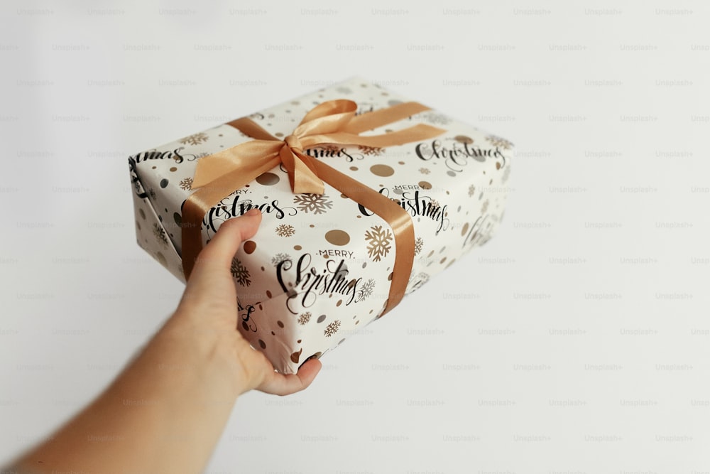 Isoliertes weißes Weihnachtsgeschenk eingewickelt in Papier und goldenes Band, verpacktes Geschenk in der Hand auf isoliertem weißen Hintergrund, Grußkartenkonzept