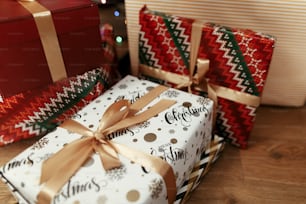 Christmas presents wrapped in colorful gift boxes and golden ribbons, lying on the wooden floor background under green christmas tree with silver ornament decoration, greeting card concept