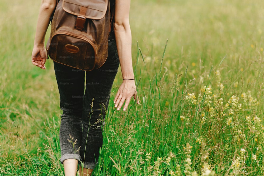 stilvolle Hipster-Frau, die im Gras spazieren geht und Kräuter-Wildblumen in den Sommerbergen in der Hand hält, Reisekonzept, friedlicher Entspannungsmoment