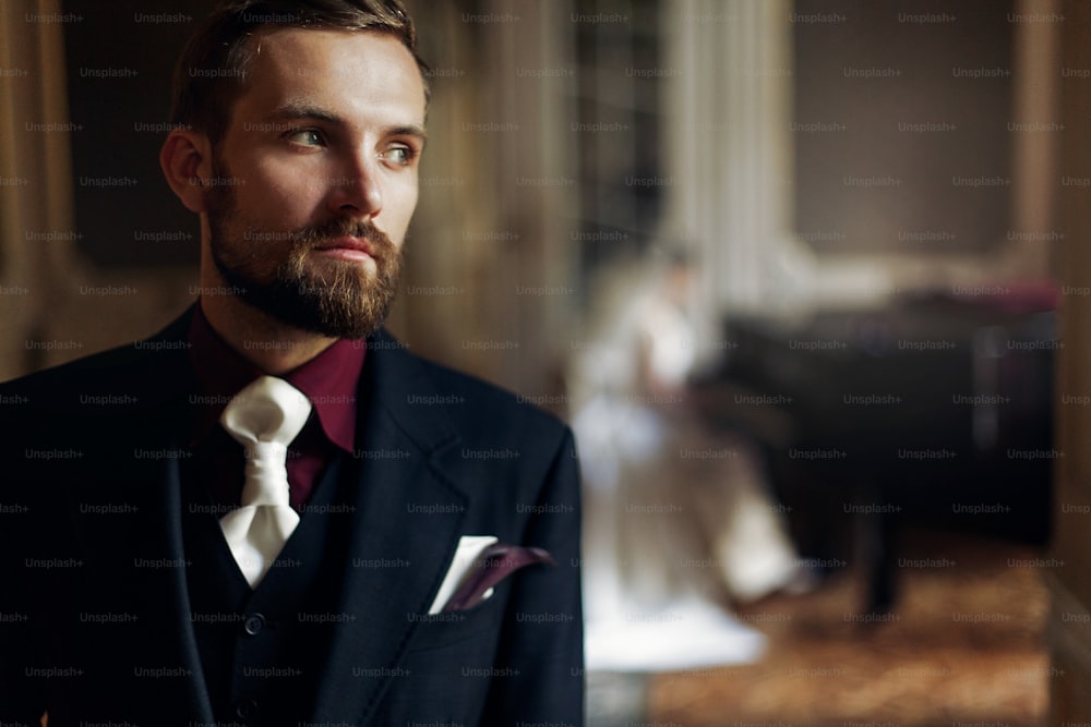 elegant stylish handsome groom listening to his gorgeous bride playing the fortepiano. unusual luxury wedding couple in retro style