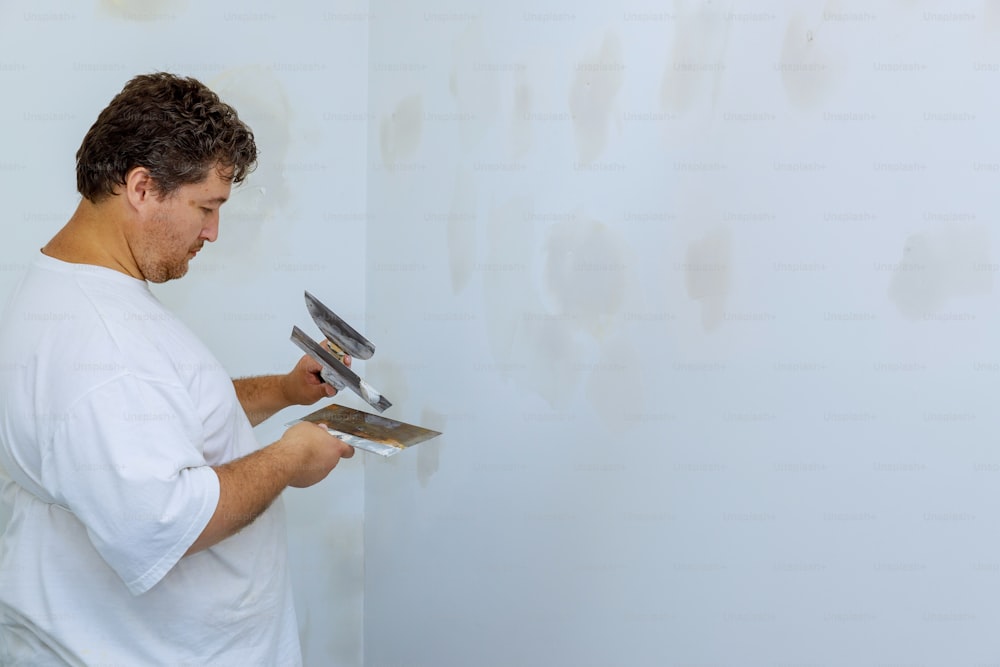 Primer plano de un hombre alineando una pared con espátula y enlucido de una pared de cartón yeso
