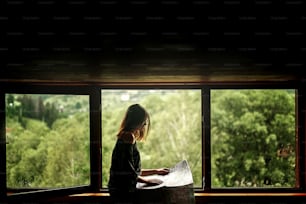 Frau hält Karte sitzt am Fenster mit Blick auf erstaunliche Berge im Holzhaus, Planung Sommerreise oder Architektenkonzept, Platz für Text