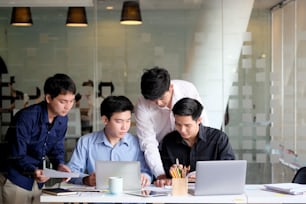 Group of Asian coworkers discussing something on a laptop in office.