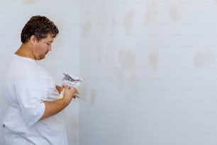 Arbeiter, der mit Spachtel- und Spachtelarbeiten arbeitet, richtet sich an der Wand aus
