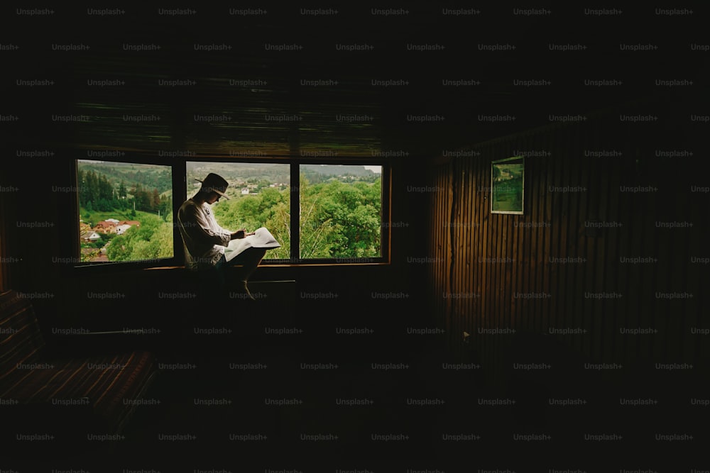 세련된 힙스터 남자는 창가에 앉아 산을 바라보며 지도를 들고 목조 주택, 여름 여행 컨셉, 텍스트 공간을 탐험합니다.