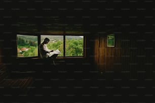 stylish hipster man sitting at window with view on mountains and holding map and exploring in wooden house, summer travel concept, space for text