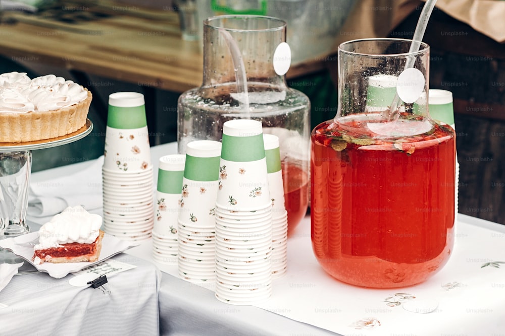 lemonade with strawberry and mint in big glass jars and paper cups, space for text. street food festival. drink bar at reception, catering outdoors. summer picnic. colorful drinks